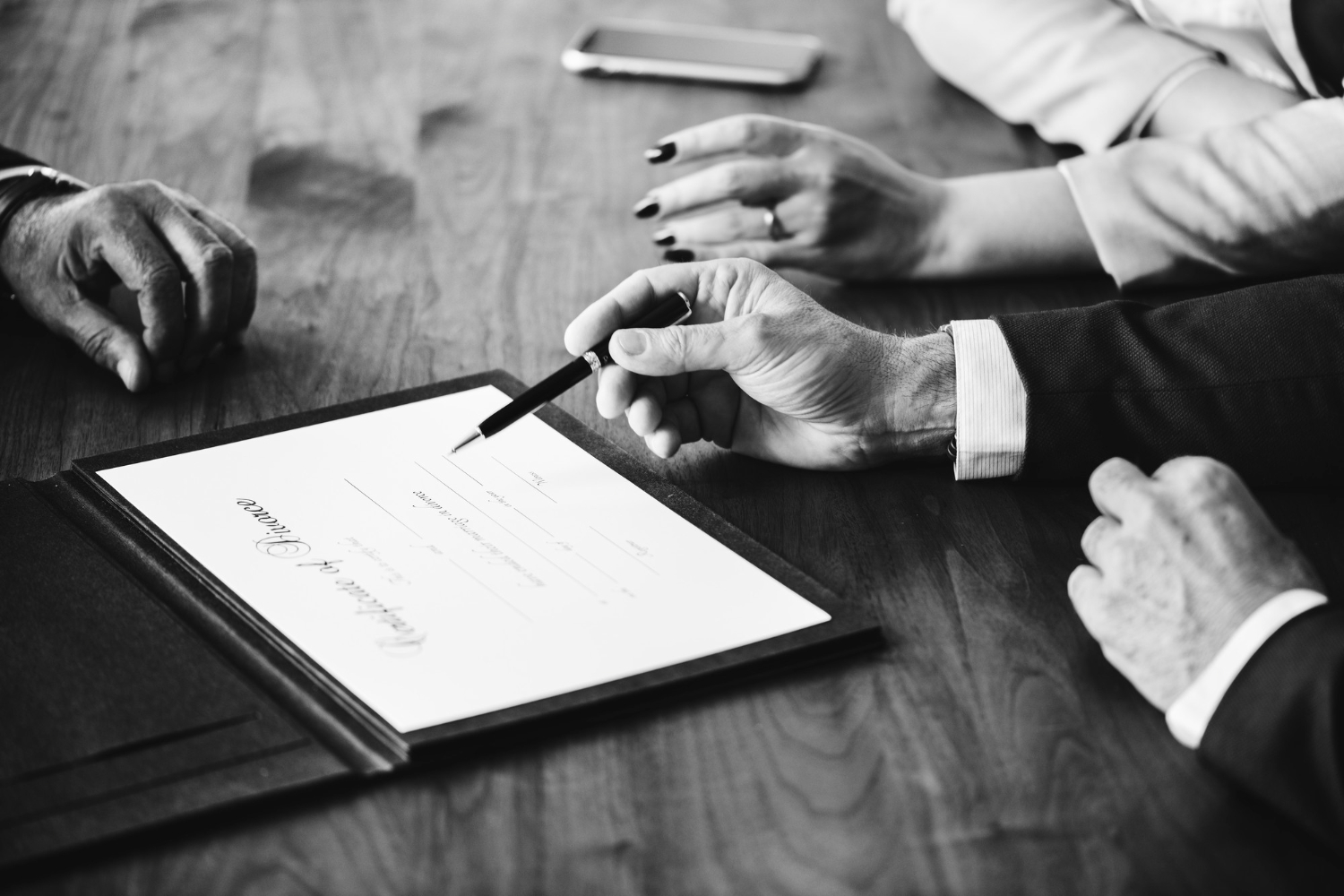 Close-up of hands holding a pen over a marriage certificate on a wooden table.