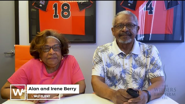 Alan and Irene Berry sit side by side at a table with framed sports jerseys in the background.