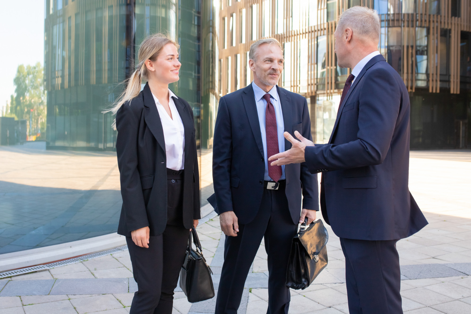 Three business professionals in suits standing and conversing outside a modern office building.