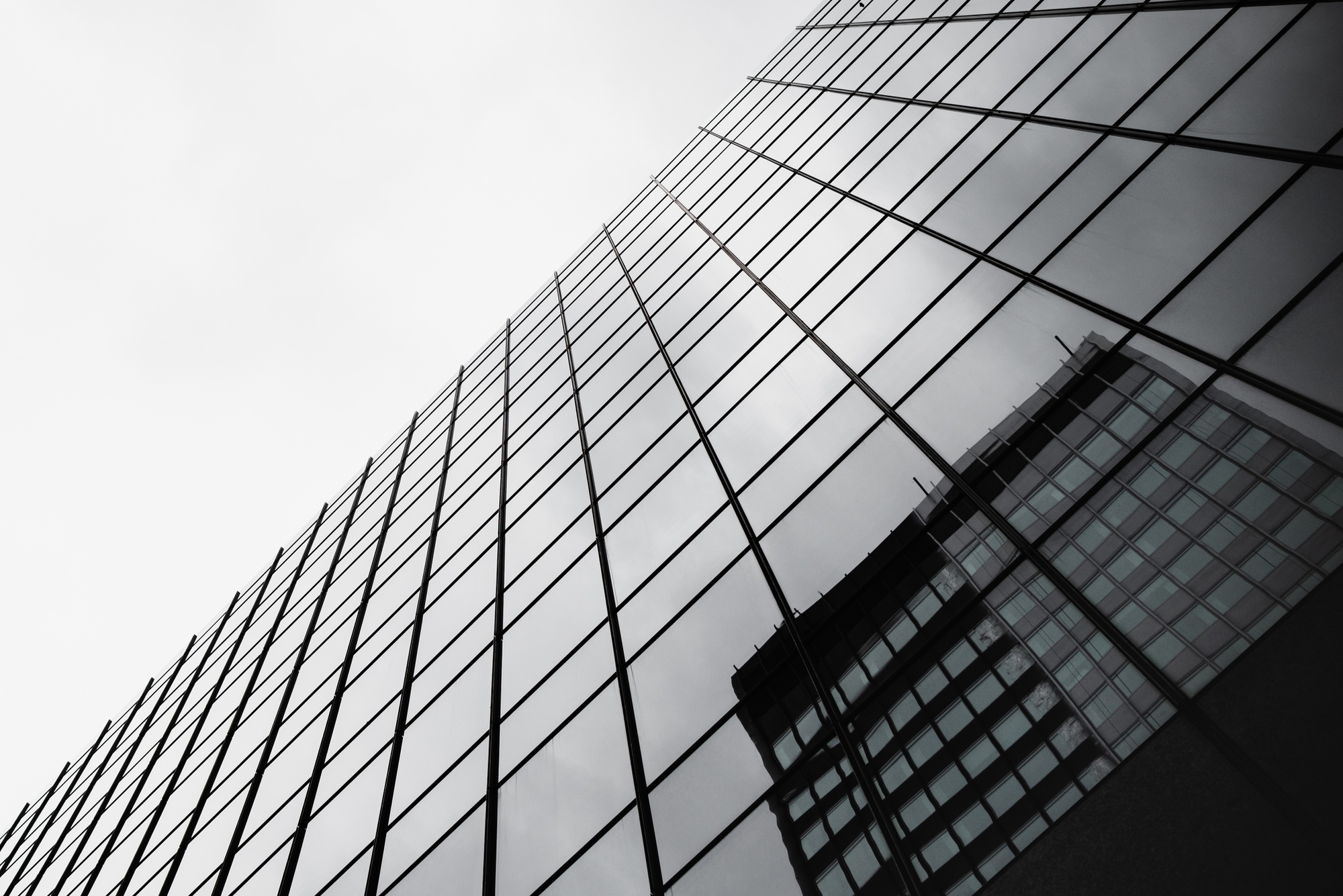 Reflection of a modern glass building on the mirrored facade of another high-rise building.